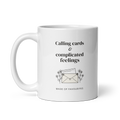 White 11 oz mug with handle on the left, showing Calling cards & complicated feelings lettering with a floral envelope. Supplier-generated mockup; not a physical sample.